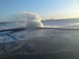 Eine Welle bricht sich am Steg